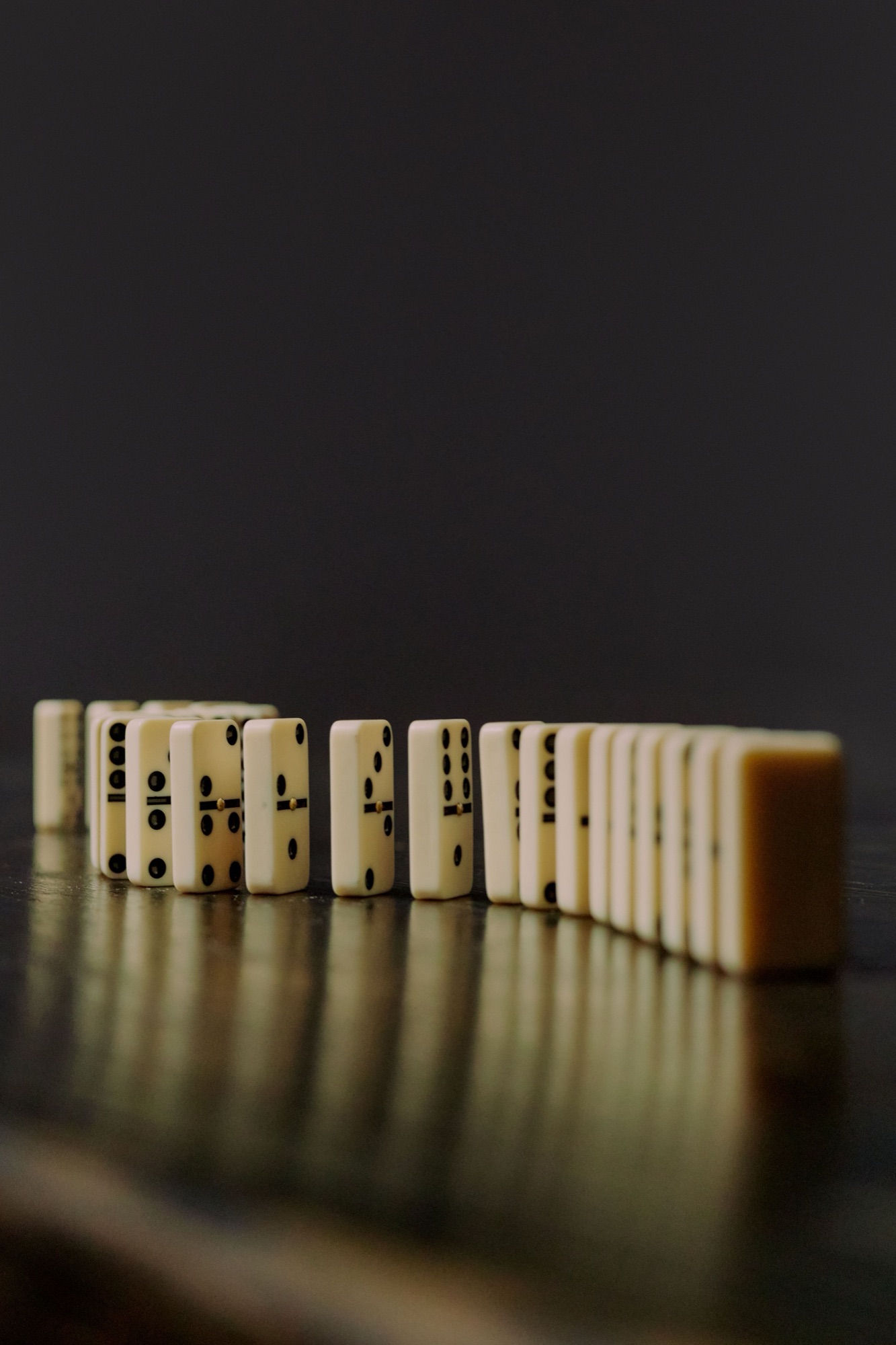 Rangée de dominos ivoire dressés sur une surface sombre et réfléchissante.